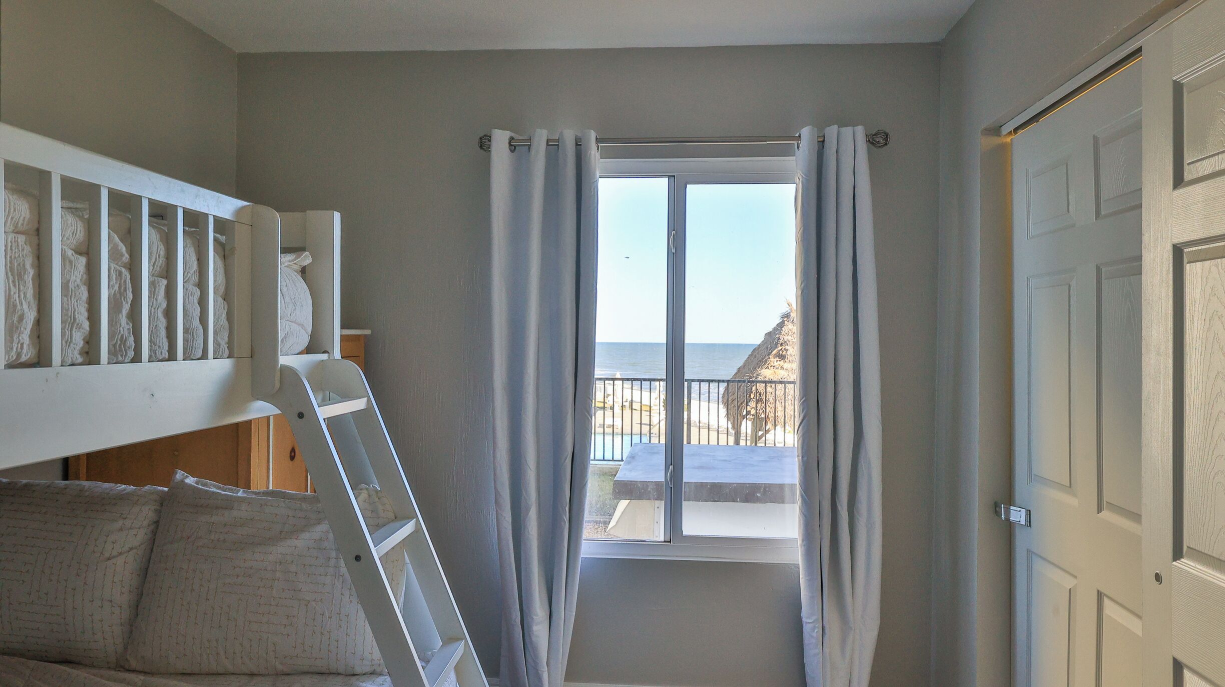 Une chambre avec vue sur la mer, un lit blanc, une échelle et une porte.