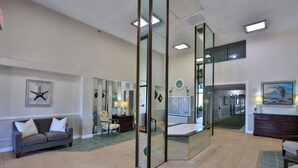 A spacious living room with a gray sofa, a green area rug, and a large mirror reflecting the room. - Coastal Charm, 1stFL Stunning Oceanfront 2BR Condo, Lg Balcony, Pool (Daytona Beach)