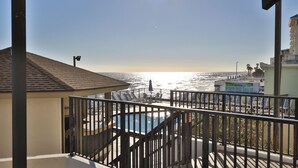 A balcony with a view of the ocean, a pool, and a beach area with lounge chairs. - Coastal Charm, 1stFL Stunning Oceanfront 2BR Condo, Lg Balcony, Pool (Daytona Beach)