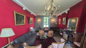 Una habitación con pared roja, candelabro, piano y varias sillas.