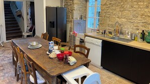 Una cocina rústica con una mesa de madera, sillas, un refrigerador, un fregadero y una pared de piedra.