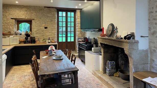 Una cocina rústica con pared de piedra, vigas de madera, un ventanal grande y una chimenea.