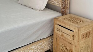 A bed with a patterned headboard and footboard, a bedside table with intricate carvings, and a simple white bedspread. - RIAD Beautiful Places  (Tahannaout)