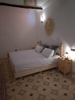 A bedroom with a bed, nightstand, wall-mounted lamp, and patterned floor tiles.
