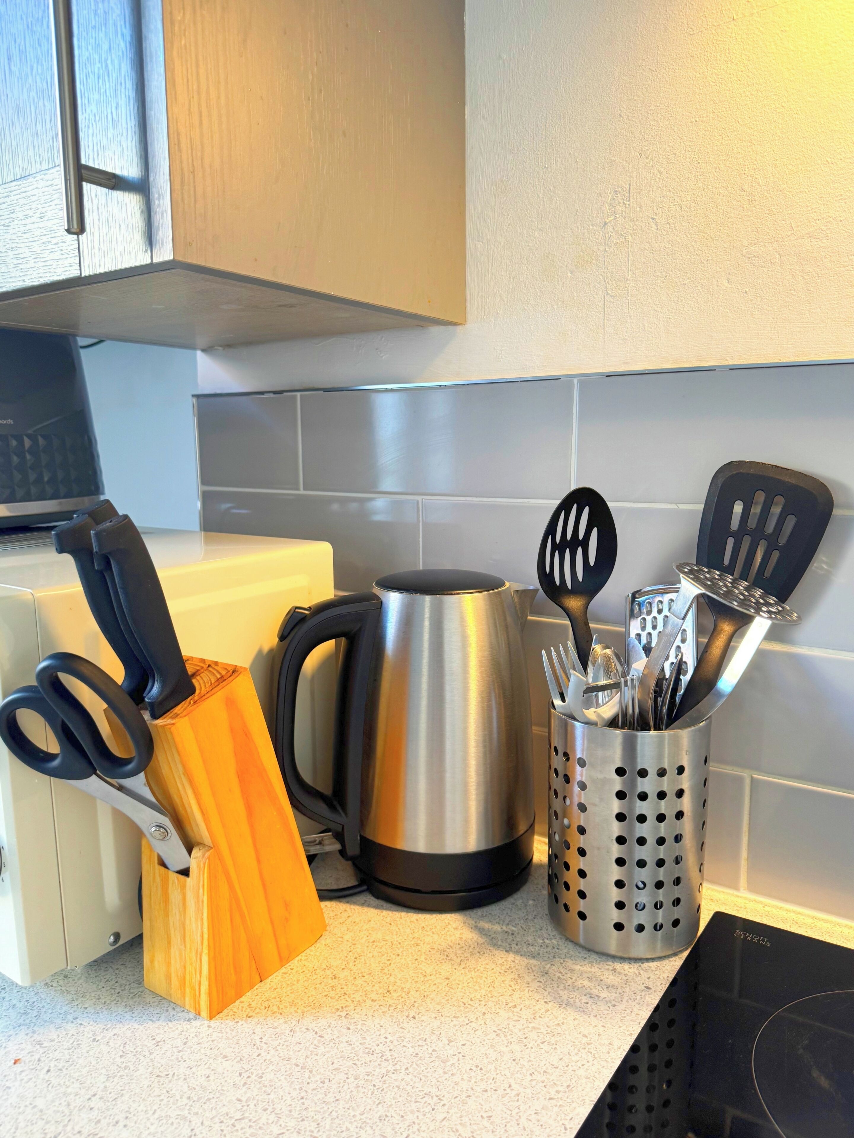A kitchen counter with a kettle, a knife block, and a utensil holder.