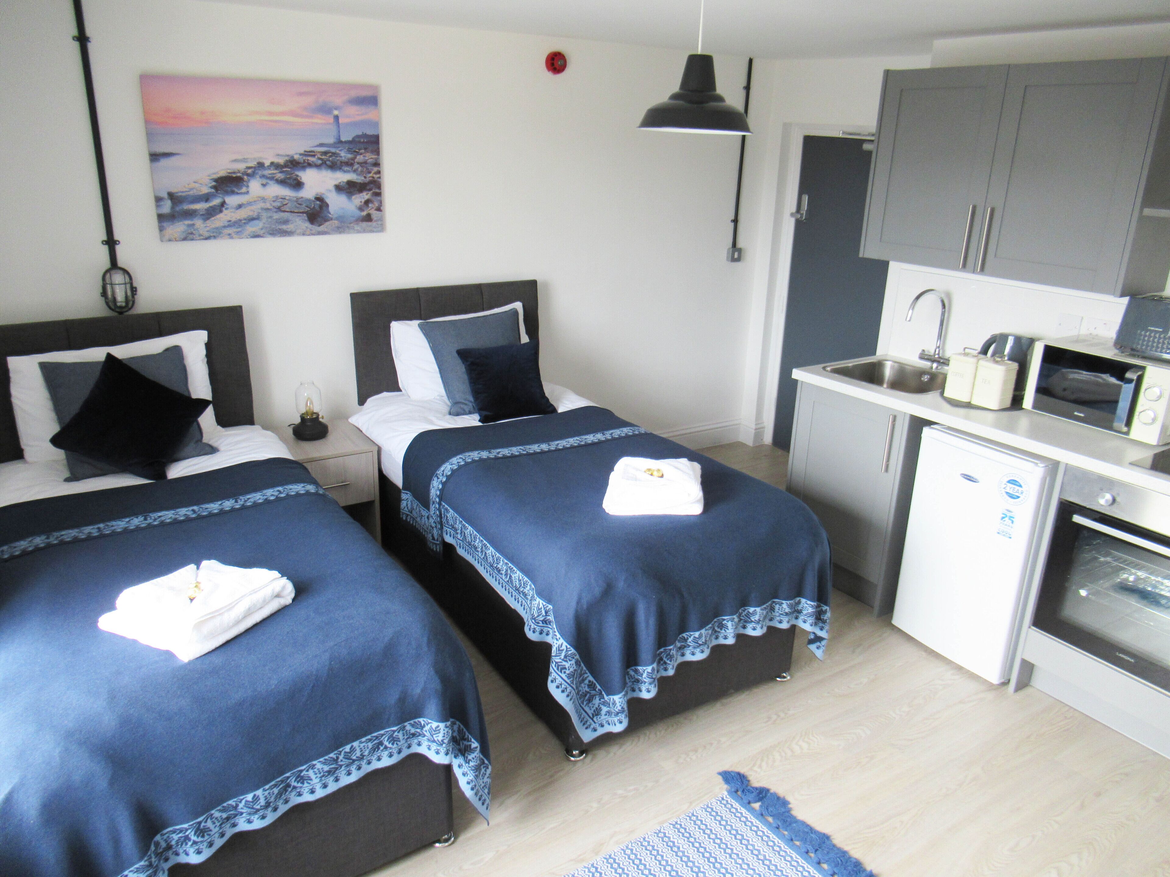 A hotel room with two beds, a small kitchenette, and a painting on the wall.
