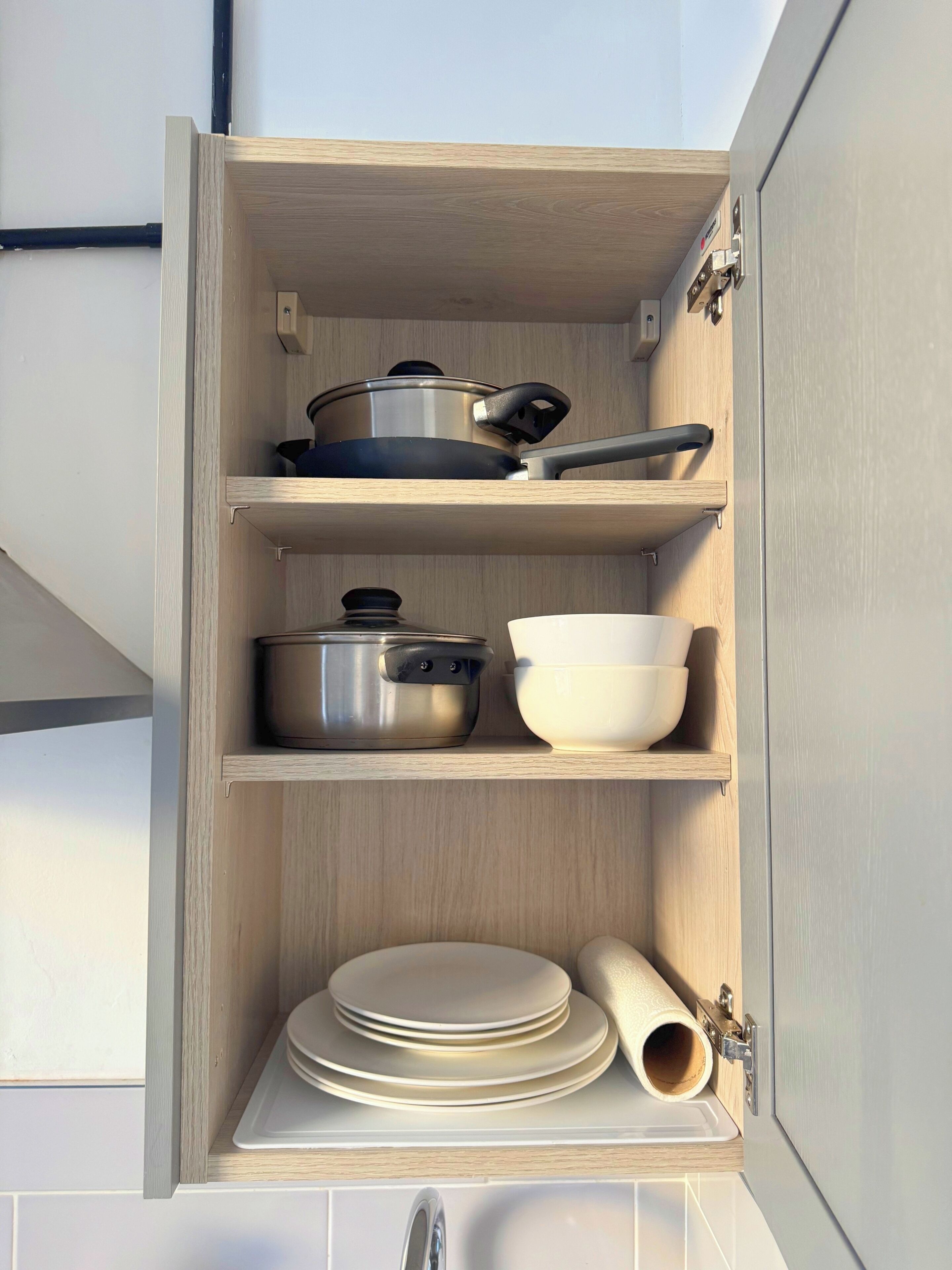 A kitchen cabinet with shelves holding cookware, bowls, plates, and a rolling pin.
