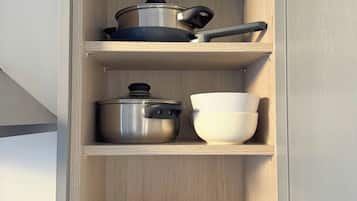 A kitchen cabinet with shelves holding cookware, bowls, plates, and a rolling pin.