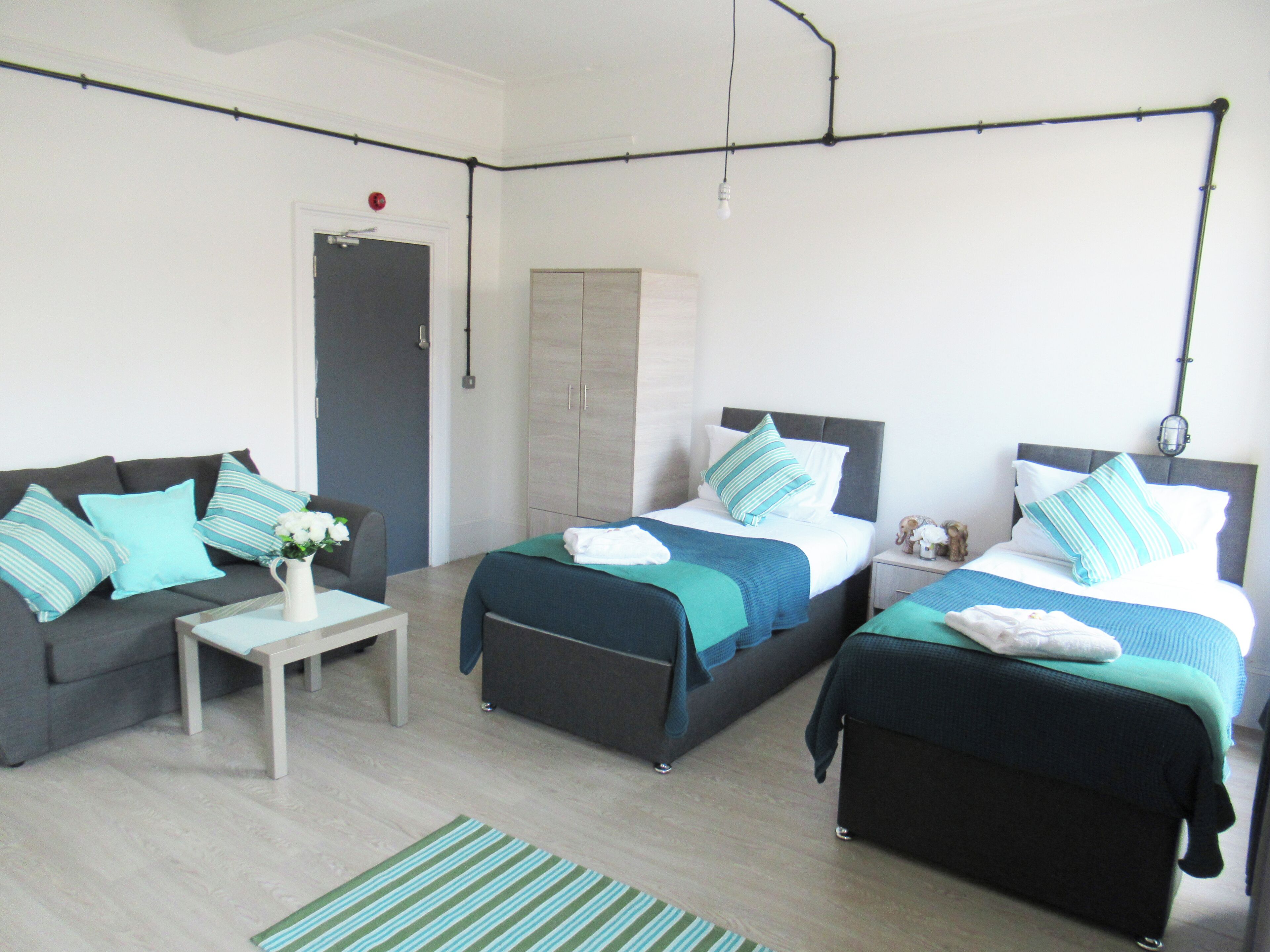 A modern, well-lit room with two beds, a sofa, and a small table.