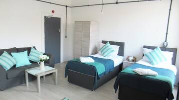 A modern, well-lit room with two beds, a sofa, and a small table.