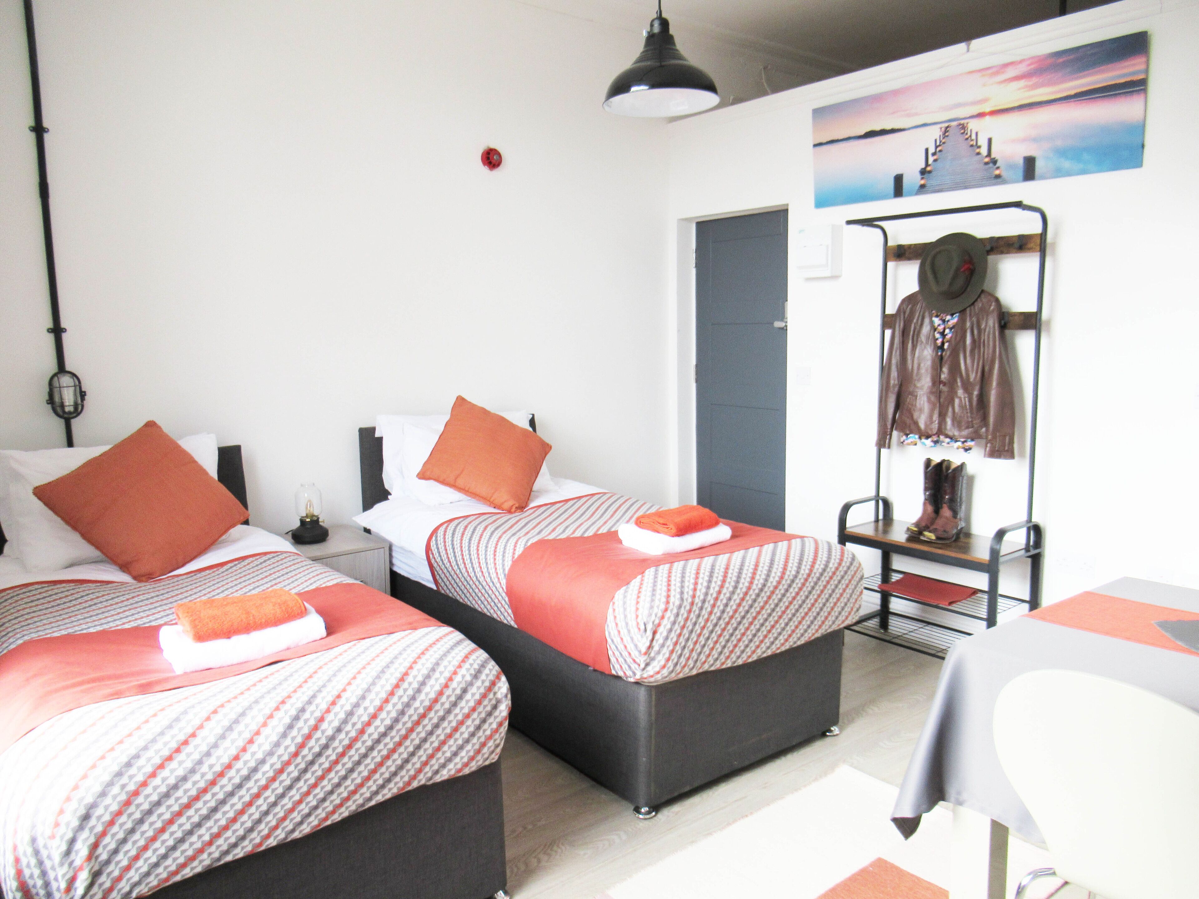 A hotel room with two beds, a wardrobe, a table, and a hanging coat rack.