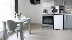 A modern kitchen with a dining area, a TV mounted on the wall, and a small oven. - Queen Street Apartments (Wolverhampton)