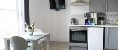 Una cocina moderna con comedor, televisor montado en la pared y horno pequeño.