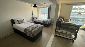 A modern bedroom with two beds, a small seating area, and a large window offering a view of buildings. - Queen Street Apartments (Wolverhampton)