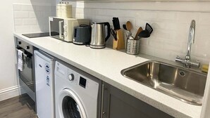 A compact kitchen with a stainless steel sink, a washing machine, a coffee maker, and a kettle. - Queen Street Apartments (Wolverhampton)