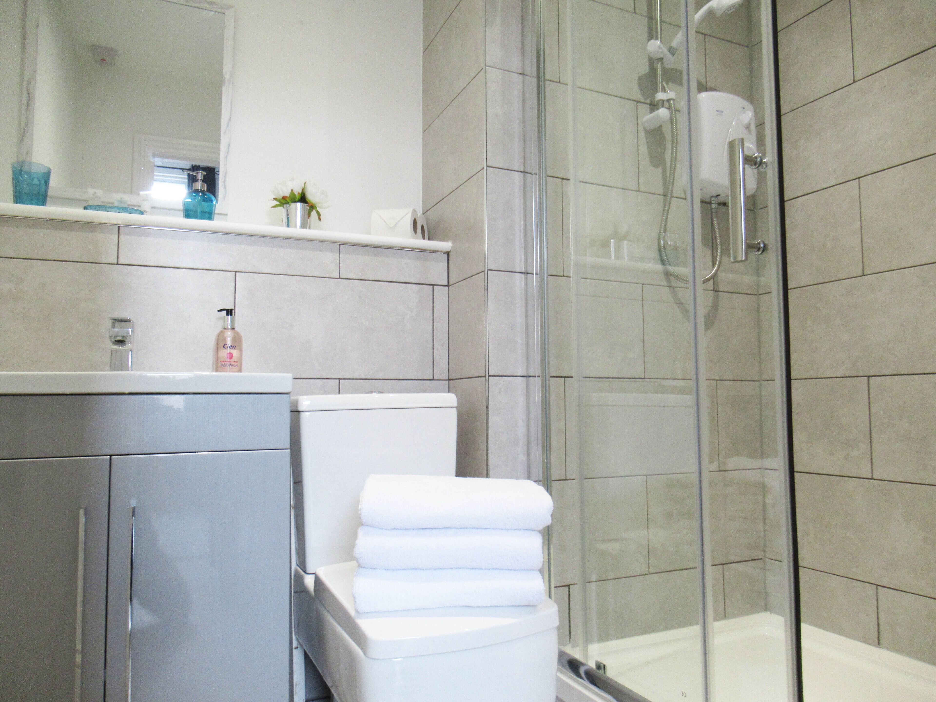 Une salle de bain moderne avec une douche à parois de verre, des toilettes et un lavabo surmonté d’un miroir.