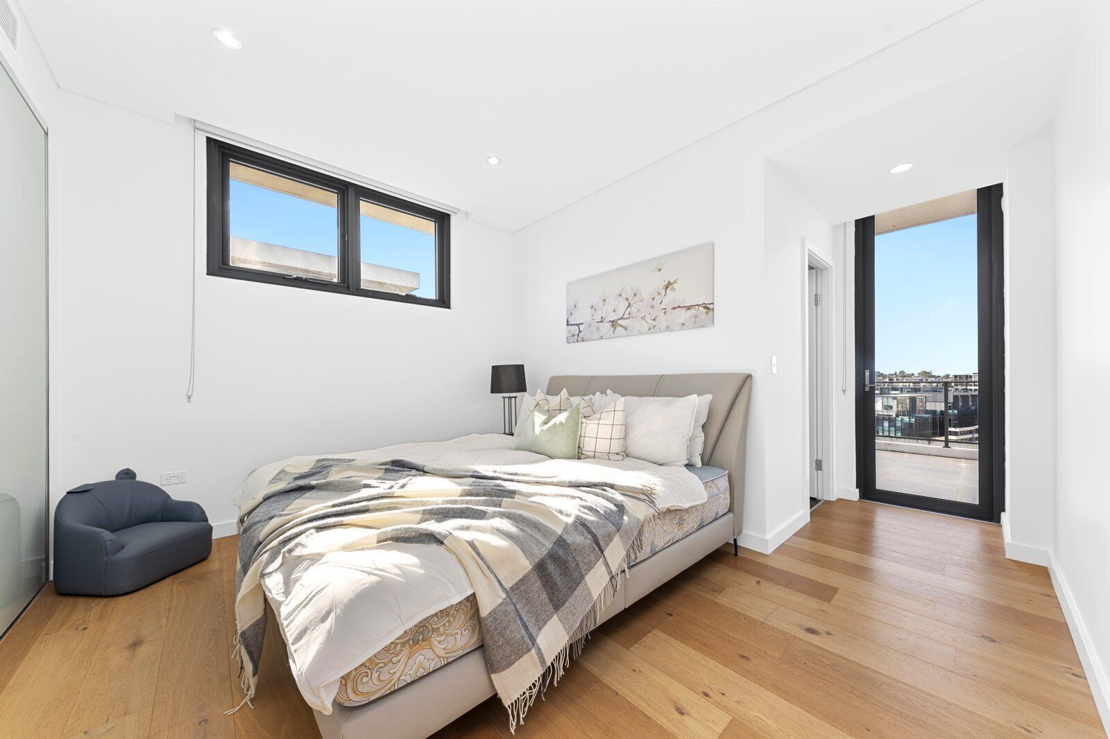 Une chambre moderne avec un grand lit, une chaise, une fenêtre et une porte donnant sur un balcon.