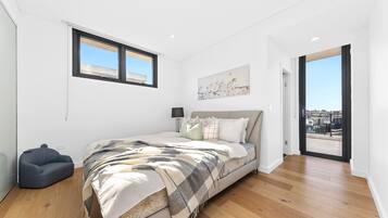 A modern bedroom with a large bed, a chair, a window, and a door leading to a balcony.