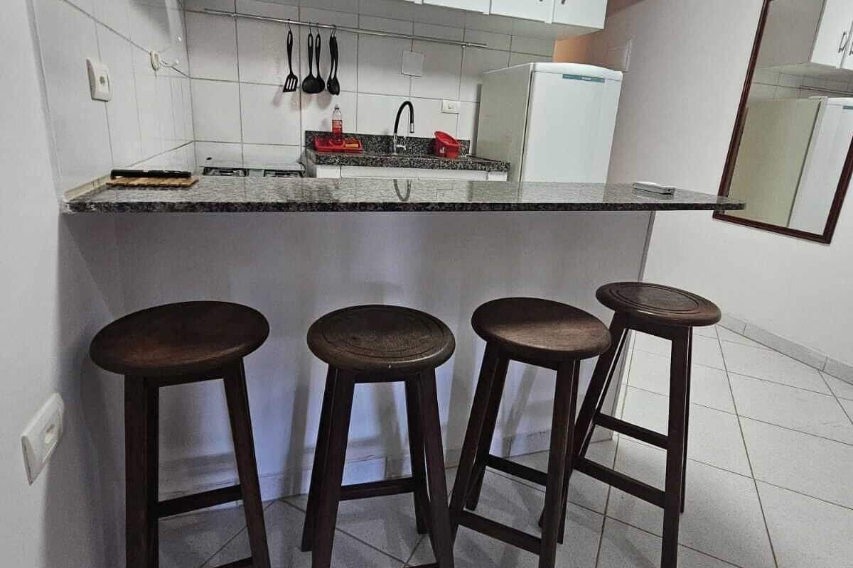 Une cuisine de taille réduite avec des meubles blancs, un plan de travail en granit, un évier et trois tabourets en bois.