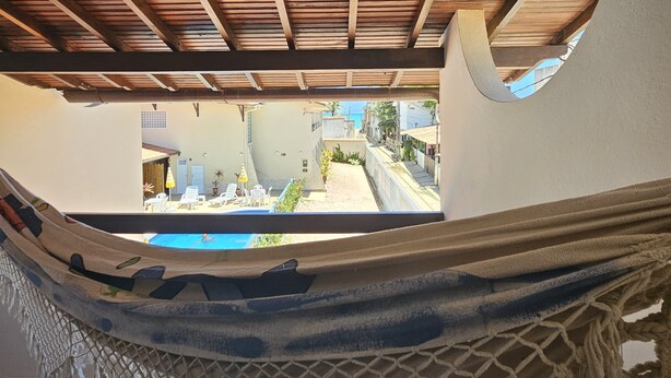 A hammock under a wooden ceiling with a view of a pool and outdoor seating. - Suites Pontal dos Golfinhos (Ipojuca)