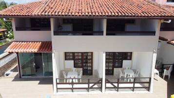 A two-story building with a tiled roof, a glass door entrance, and a balcony with white plastic chairs.