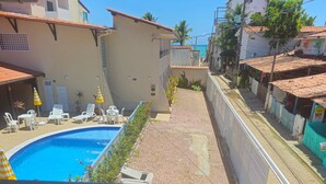 A residential area with a swimming pool, white lounge chairs, and a tiled roof. - Suites Pontal dos Golfinhos (Ipojuca)