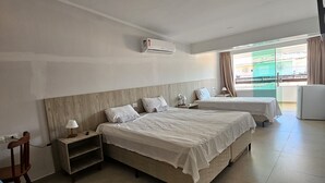 A bedroom with a large bed, a smaller bed, a nightstand, a chair, and a window with curtains. - Suites Pontal dos Golfinhos (Ipojuca)