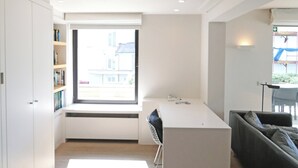 Eine moderne Küche mit einem großen Fenster, einem Essbereich mit weißem Tisch und Stühlen sowie einem grauen Sofa.