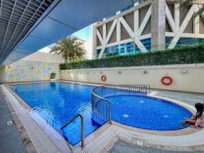 Ein Schwimmbecken mit geometrischem Fliesendesign, einem Rettungsring und einem Kind, das am Beckenrand sitzt.