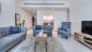 A modern living room with a grey sofa, armchair, and ottoman, a coffee table, and a TV on a wooden stand. - Chic Marina Arcade Apartment Minutes to Beach (Dubai)