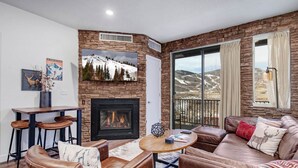 A cozy living room with a fireplace, leather furniture, and a scenic mountain view through the large window. - Moose Mgmt-The Mason 3053 (Park City)