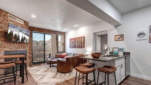A modern kitchen with a large island, bar stools, and a dining area with a view of the mountains. - Moose Mgmt-The Mason 3053 (Park City)