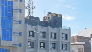Un hôtel à plusieurs étages, avec une enseigne indiquant qu’il s’agit d’un hôtel. Plusieurs voitures sont garées devant, et un lampadaire est visible.
