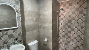 Une salle de bain équipée d’un lavabo, de toilettes et d’une douche. Les murs sont recouverts de carreaux formant un motif décoratif.