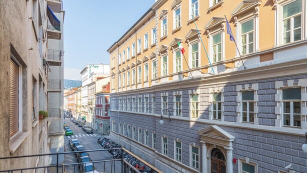 A multi-story building with a row of parked cars and motorcycles on the street below.