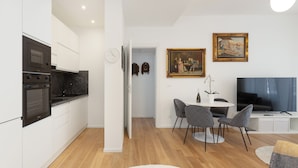 A modern kitchen with built-in appliances, a dining area with a round table and chairs, and a living space with a flat-screen TV.