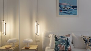A modern bedroom with a white bed, a painting of a coastal scene, and pendant lights.