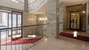 A hotel lobby with a marble staircase, a red carpet, and a glass elevator door.