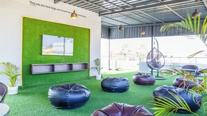 Un espace de détente intérieur avec un revêtement de sol en gazon synthétique vert, des fauteuils en forme de sac et une étagère fixée au mur.