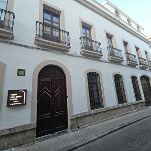 Un edificio con una entrada central amplia, múltiples ventanas con balcones y un letrero que indica la ubicación.