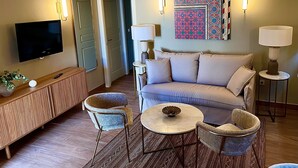 Un salon comprenant un canapé, deux fauteuils, une table basse, un téléviseur et un élément décoratif mural.