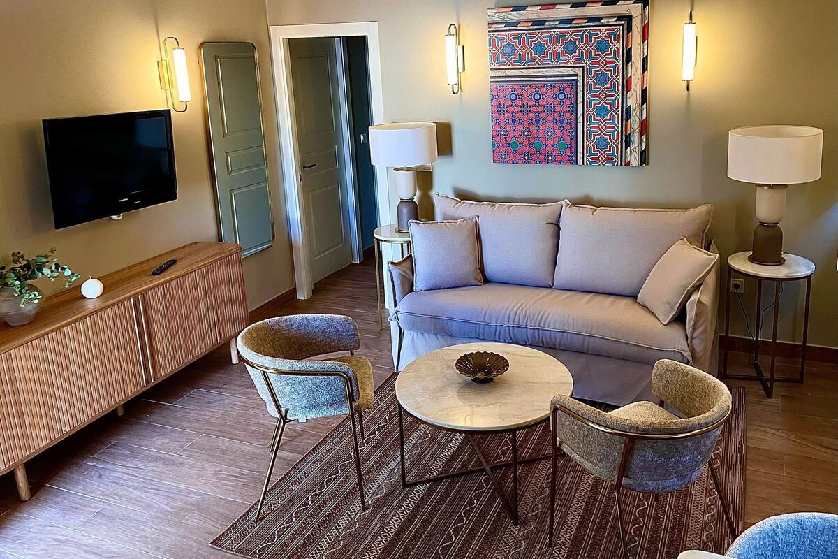 Een woonkamer met een bank, twee stoelen, een salontafel, een televisie en een decoratief kunstwerk aan de muur.