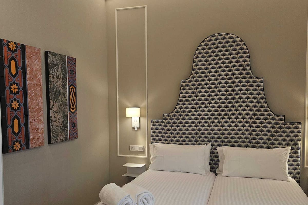 Hotelkamer met een groot bed, twee kussens, een nachtkastje, een wandlamp en drie decoratieve wandpanelen.
