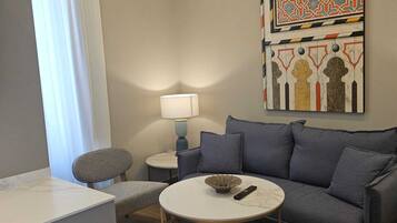 Una sala de estar moderna con un sofá gris, una mesa redonda para café y un tapete estampado. Hay una lámpara sobre una mesita auxiliar y una pieza decorativa en la pared sobre el sofá.