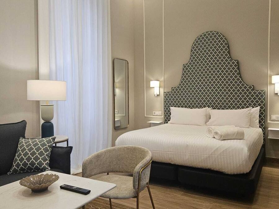 Hotellihuone, jossa on suuri sänky, työpöytä tuolilla, lamppu ja peili.