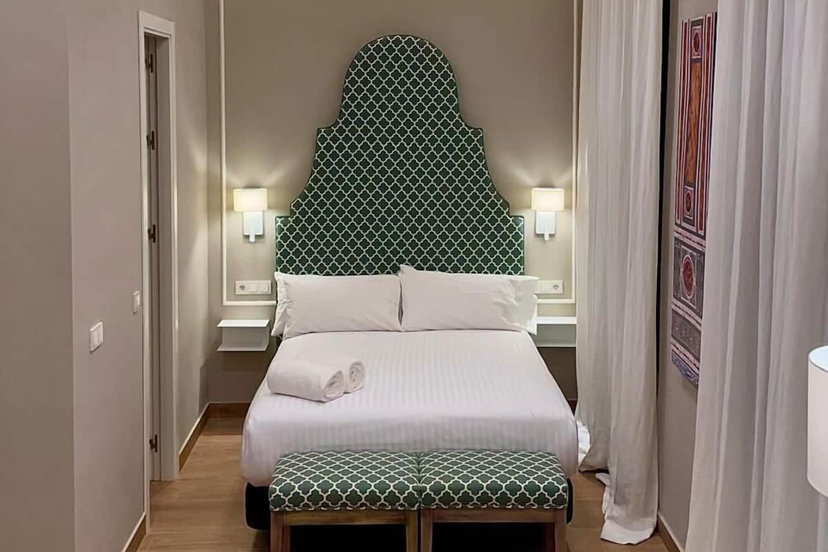 Een hotelkamer met een bed, twee stoelen, een tafel en een hoofdeinde met een geometrisch patroon.