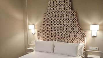 Habitación de hotel con un cabecero estampado, dos lámparas de noche, una cama bien hecha con ropa blanca y una toalla sobre la cama.