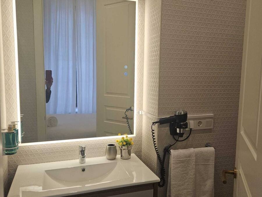 Un baño con un espejo grande, un lavamanos y un secador de pelo sobre un soporte de pared.