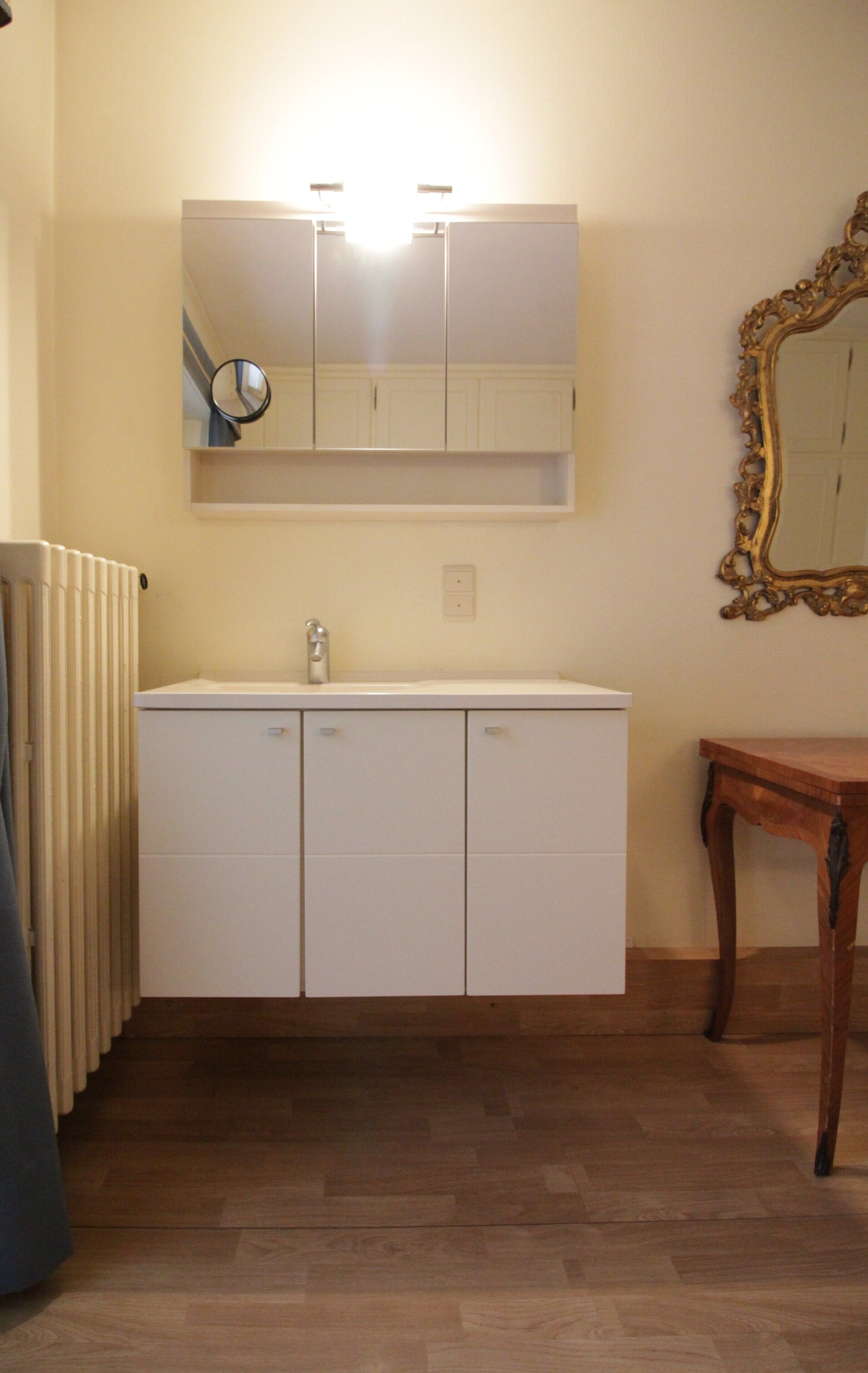 A bathroom with a white cabinet, a mirror, and a wooden table.