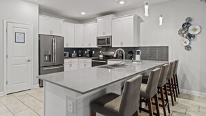 A modern kitchen with white cabinets, stainless steel appliances, and a central island with bar stools. - Spacious Villa w/ Pool, Theater & Game Room (Davenport)